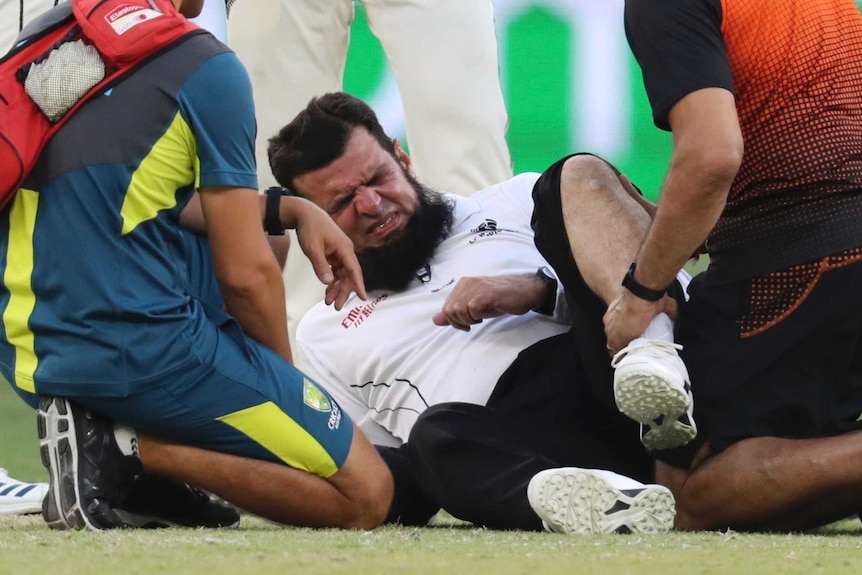 Aleem Dar grimaces while lying on the floor after a collision with a player