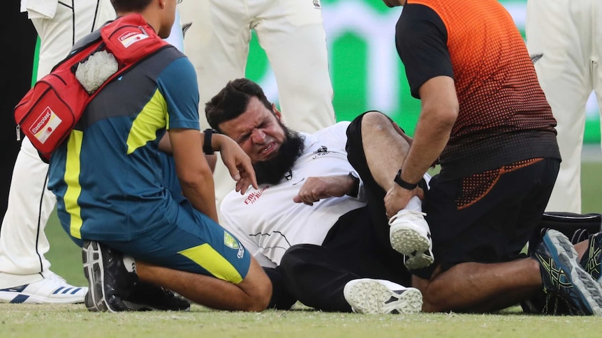 Aleem Dar grimaces while lying on the floor after a collision with a player
