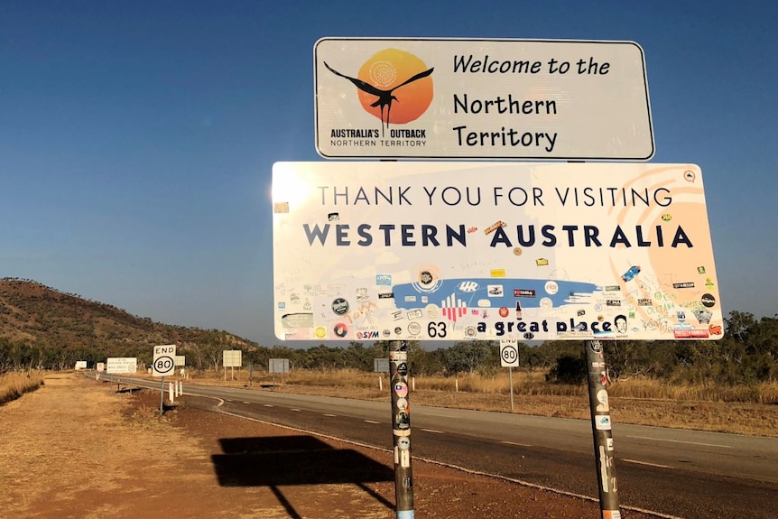 A sign says "Welcome to the Northern Territory" and "Thank you for visiting Western Australia".