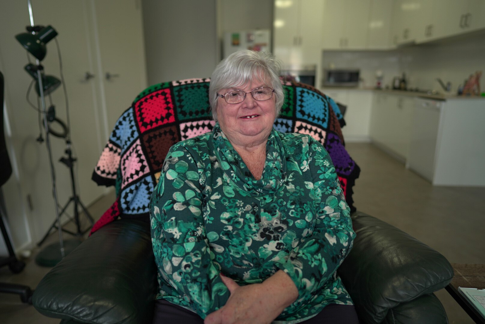 Older woman smiling wearing a green printed  shirt. 