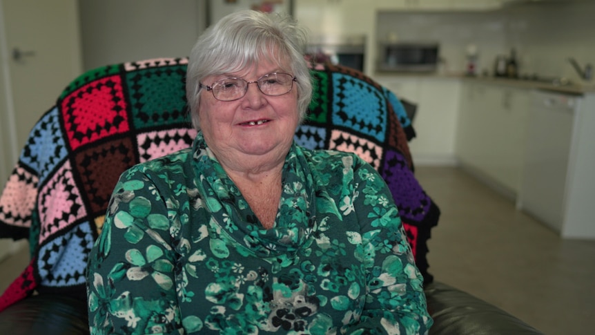 Older woman smiling wearing a green printed shirt. 