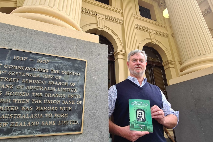 A grey-haired man stands on the steps of a historic building.