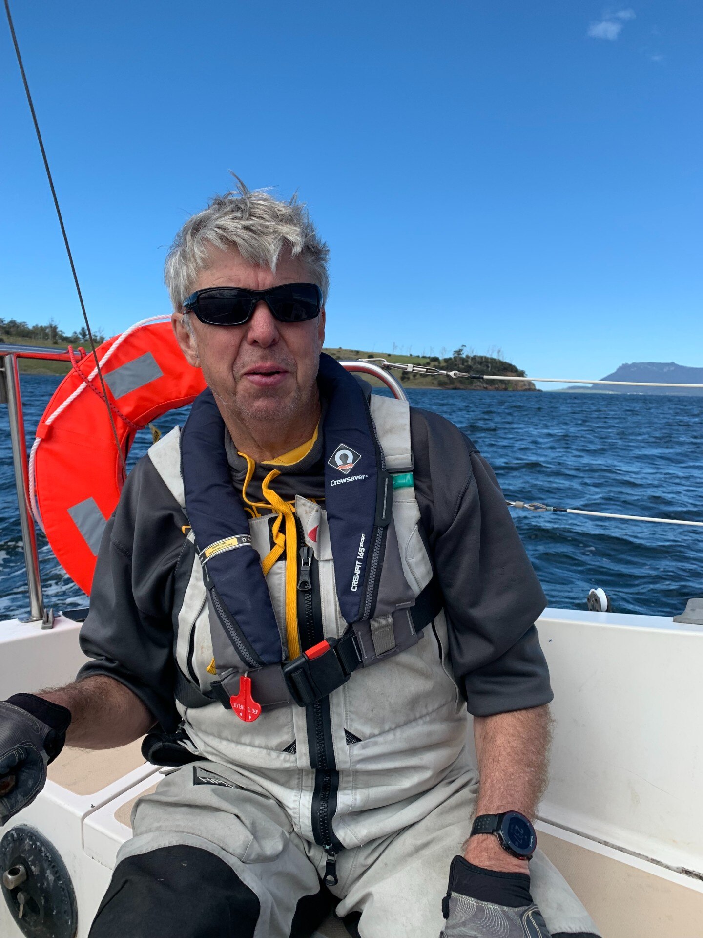 A man wearing sunglasses sits on a vessel with ocean in the background.