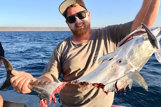 A man is holding a fish with a large bite taken out of it and smiling