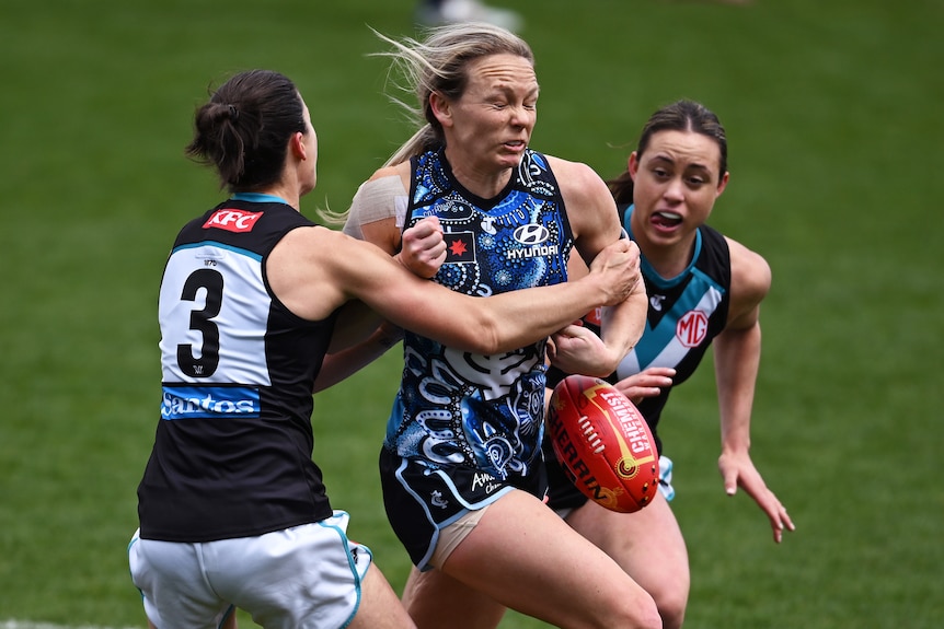 A Carlton AFLW player drops the ball while being tackled by a Port Adelaide opponent.