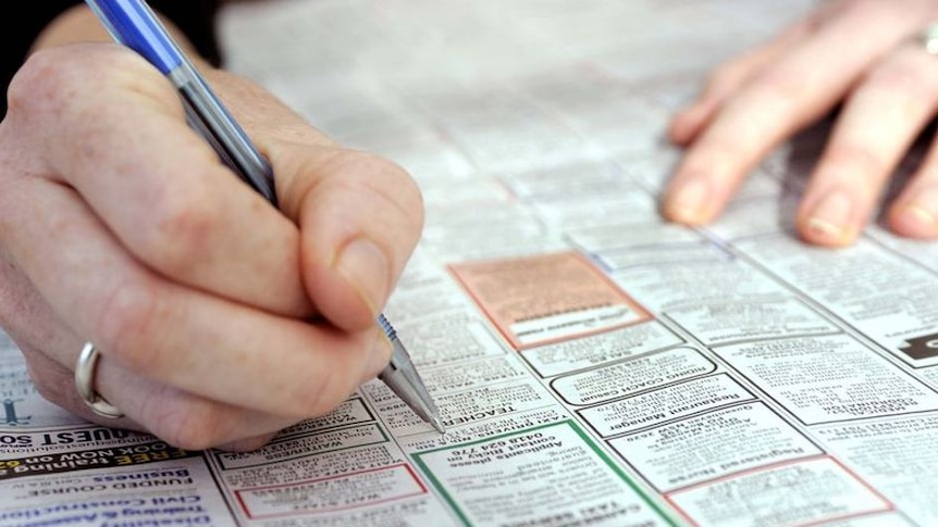 Close-up of a hand, holding a pen, circling job advertisements in the newspaper.