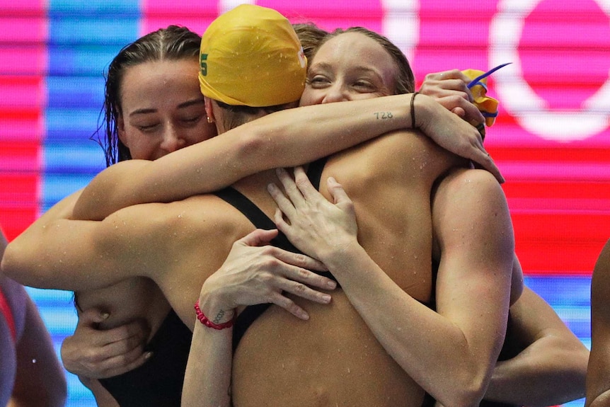 Four female swimmers hug as they celebrate breaking a world record.