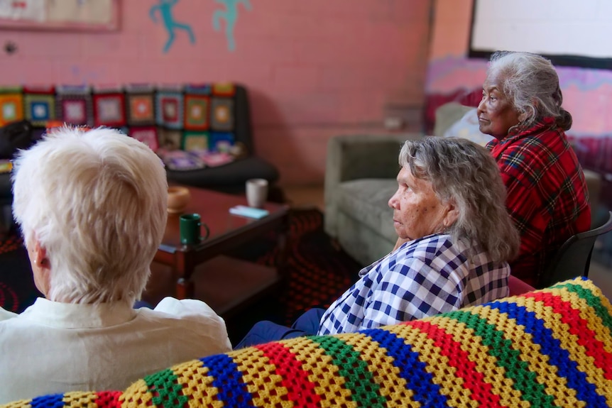 Three women in their 70s sit and listen thoughtfully on a couch.