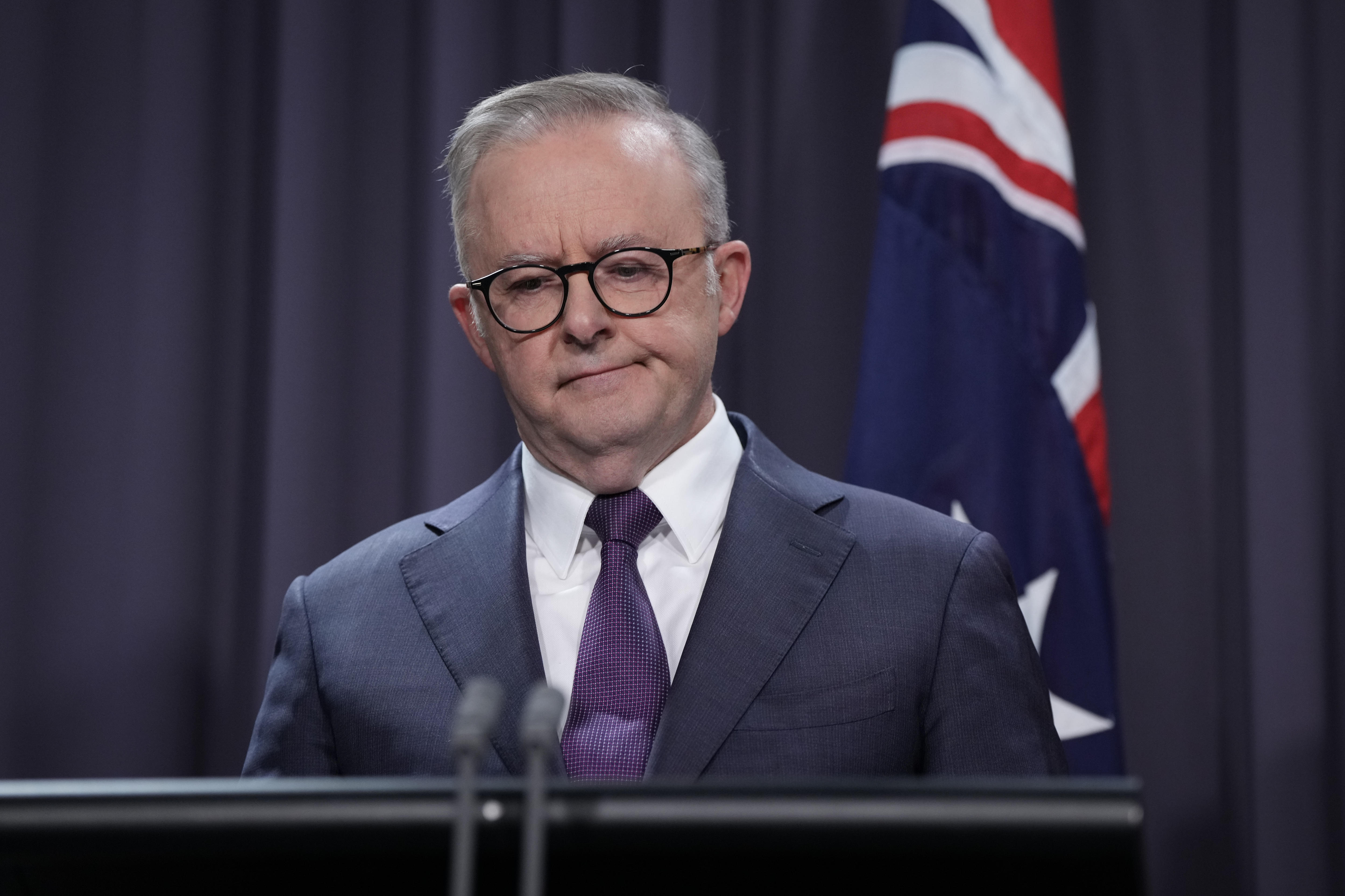 Anthony Albanese looks down and grimaces slightly during a press conference.