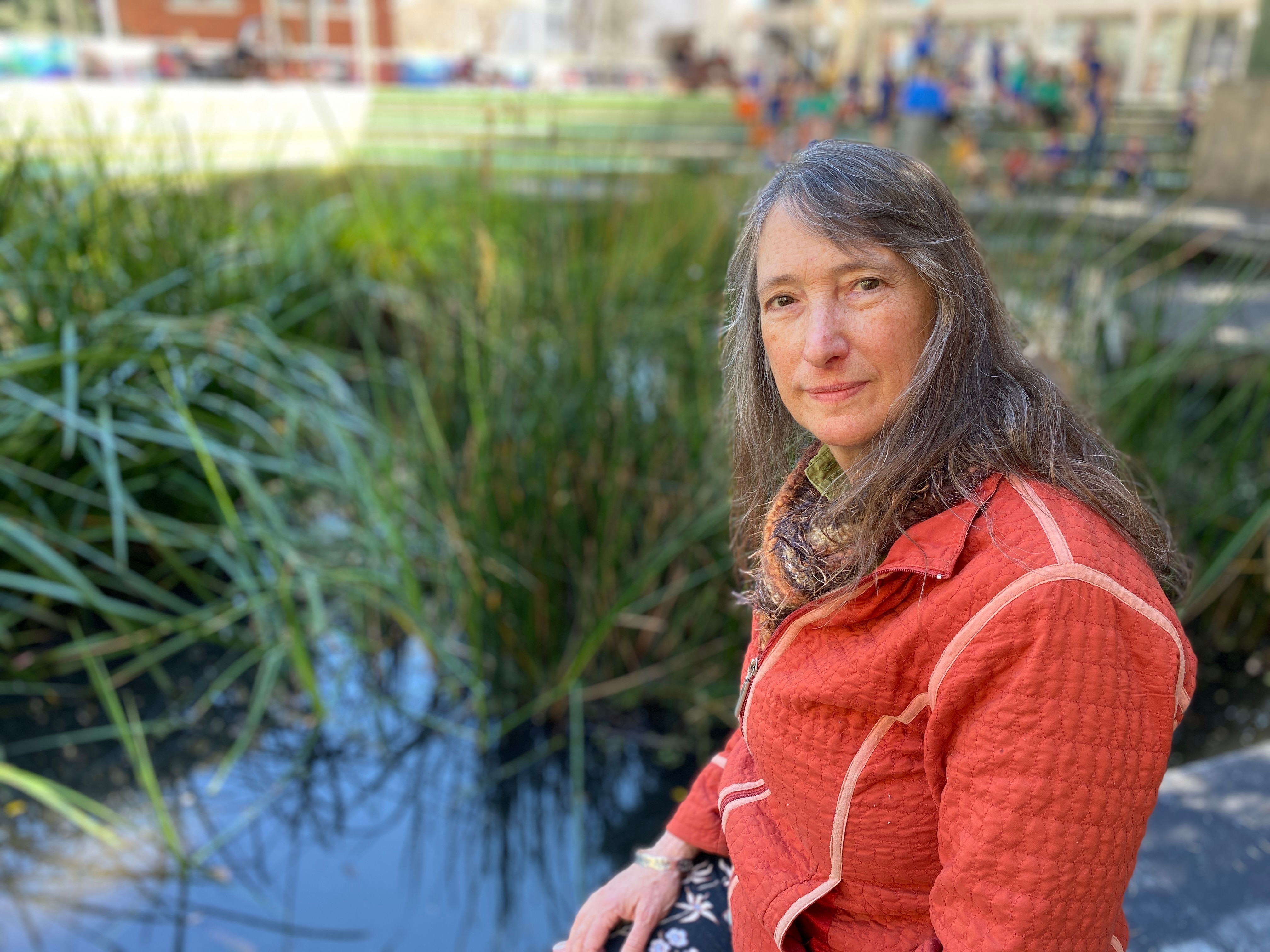 A woman looks at the camera with a blank expression. She is on the edge of a wetland