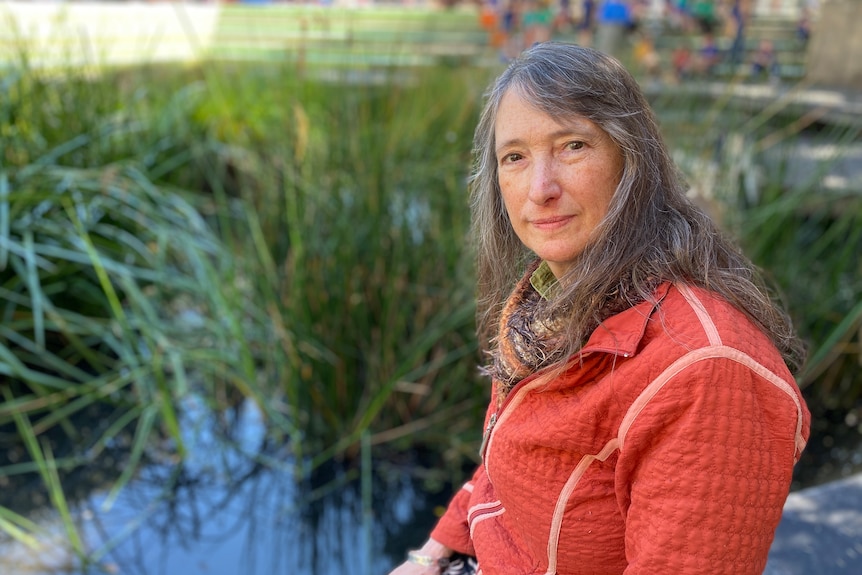 A woman looks at the camera with a blank expression. She is on the edge of a wetland
