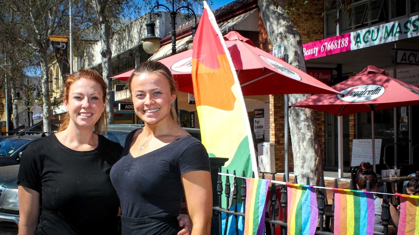 Two women stand outside a cafe flying the rainbow flags in support of same sex marriage