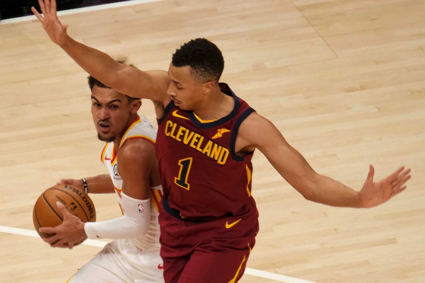 Dante Exum looks down at the ball with his arms outstretched as Trae Young holds on and peers out from under Exum's arm