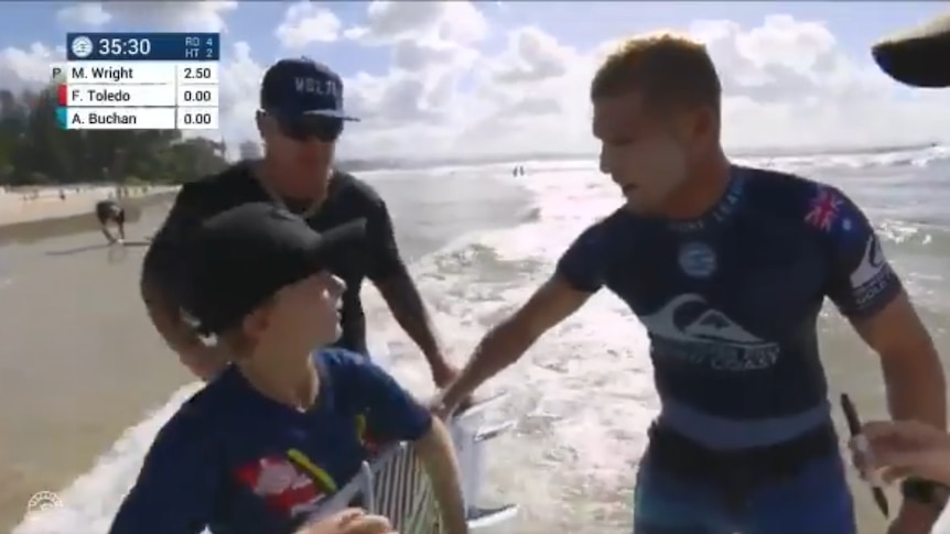 Mick Fanning gives a young fan his surfboard on the shoreline of the beach