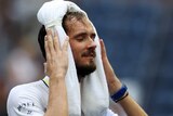 A sweaty Daniil Medvedev wraps a towel around his head with a look of relief on his face.