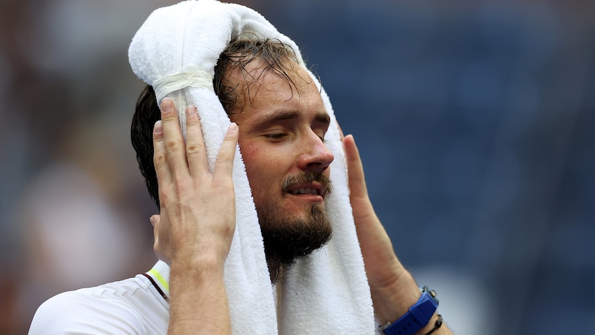 A sweaty Daniil Medvedev wraps a towel around his head with a look of relief on his face.