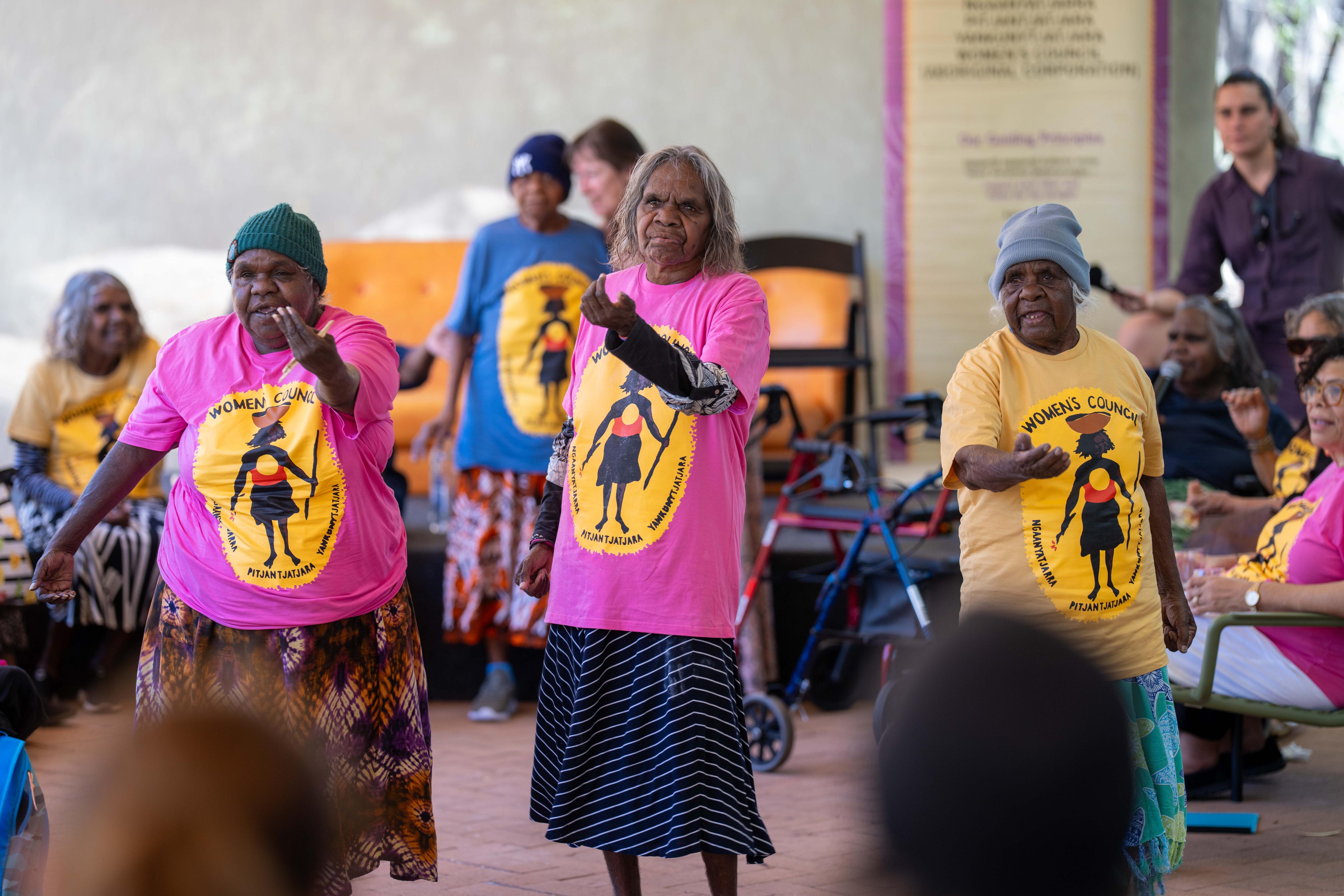 Tres mujeres se paran en fila y bailan. Llevan camisas de colores claros y parecen amigables.