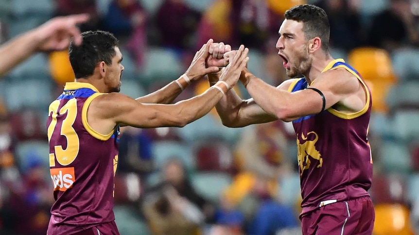 Two AFL teammates touch fists in celebration after a goal, as the player on the right roars.