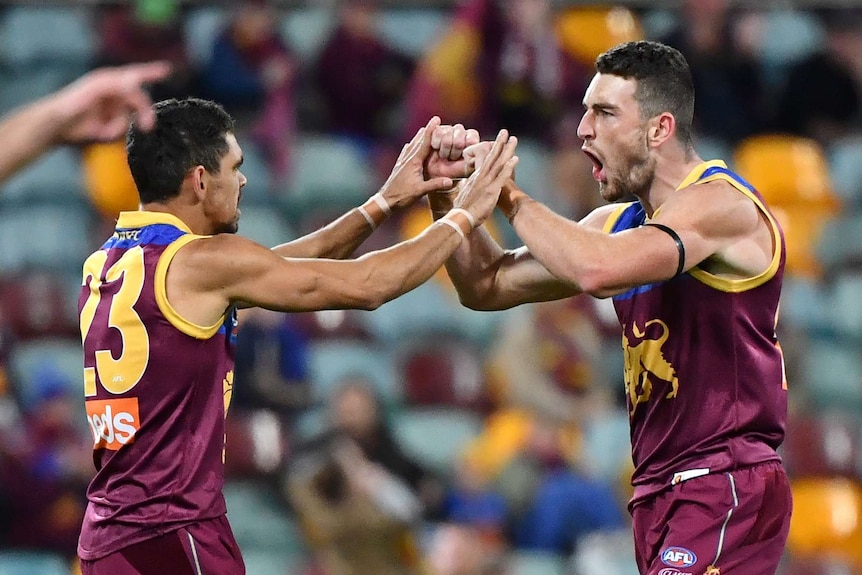 Two AFL teammates touch fists in celebration after a goal, as the player on the right roars.