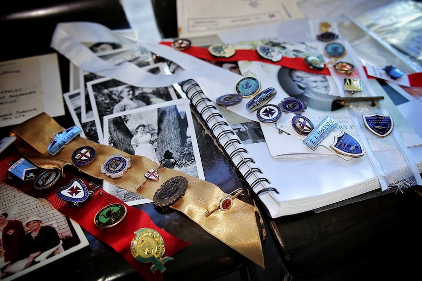 A close-up picture of old nurses' badges pinned to ribbons next to black and white pictures lying on a table.
