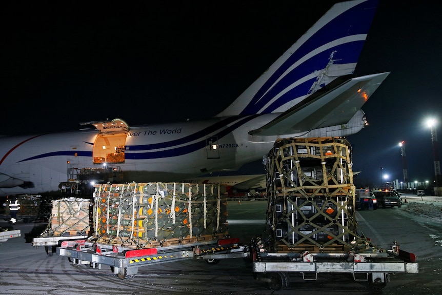 Workers unload cargo from a plane at an airport at night. 