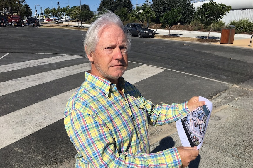 A man in his 60's in a checked shirt hold a map of a proposed development