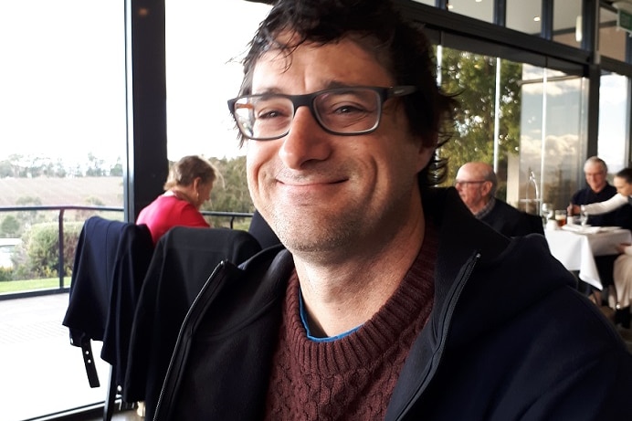 Stathi Paxinos sits in a restaurant wearing a sweater and glasses.