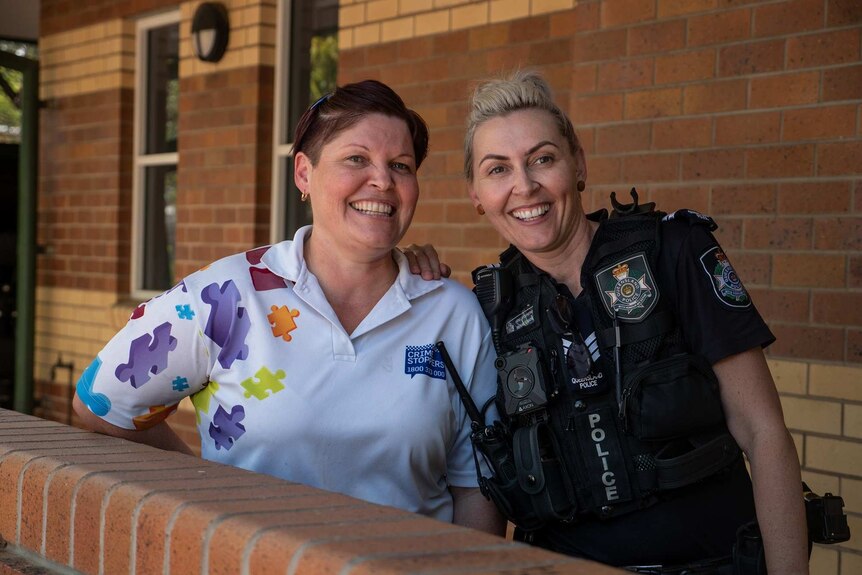Jayne Gothmann in a white Crime Stoppers shirt with colourful puzzle pieces stands with Senior Constable Renae Cannon.