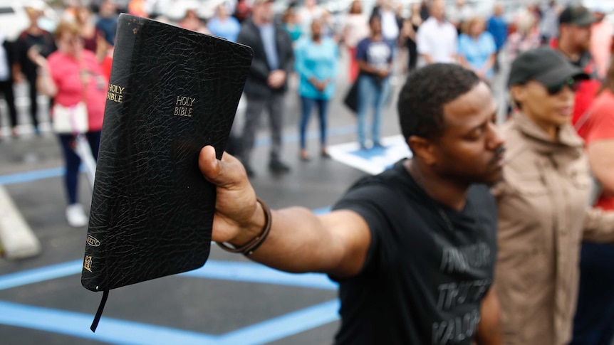 A man holds a copy of the bible in his hand, his eyes closed in prayer.
