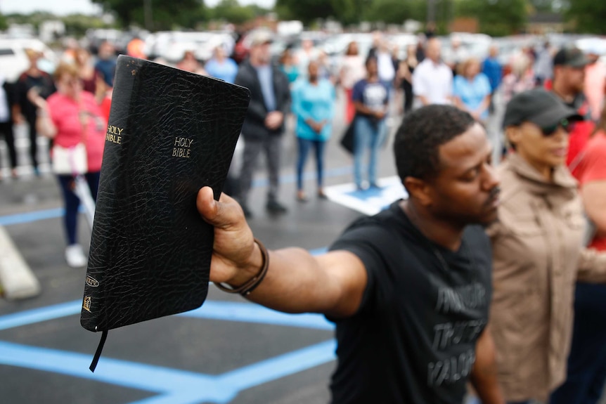 A man holds a copy of the bible in his hand, his eyes closed in prayer.