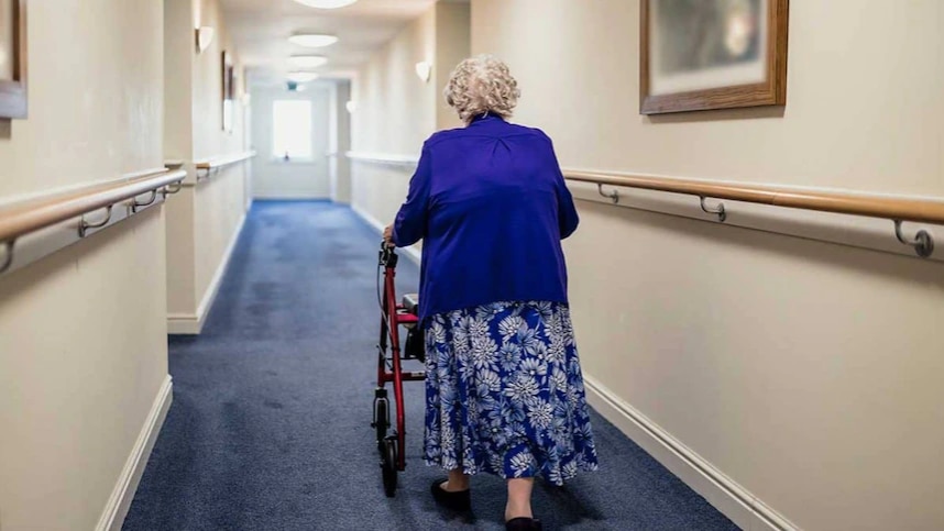 A senior person walks in a hallway with the help of a walking support tool.