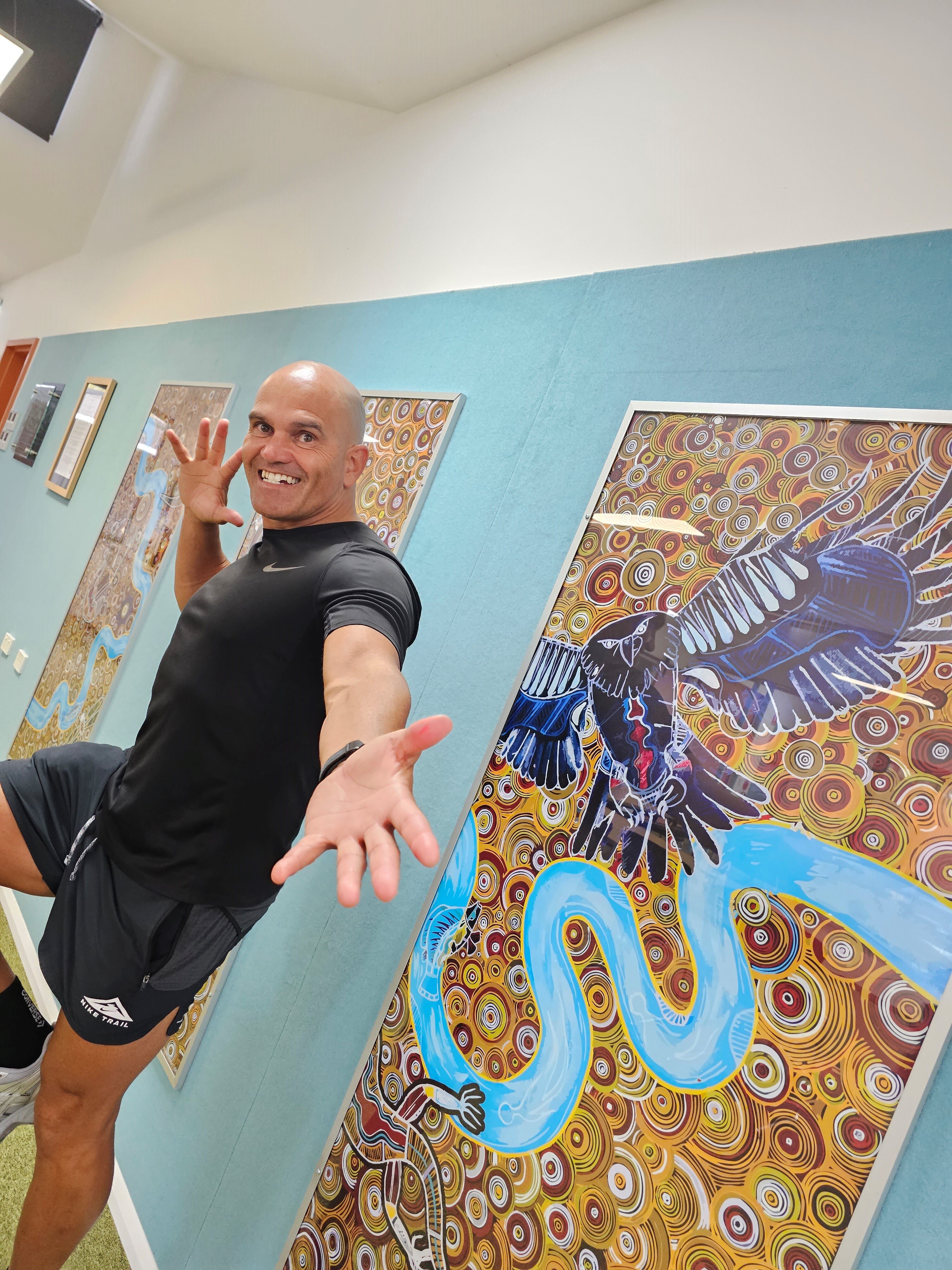 A man stans next to an Indigenous painting 