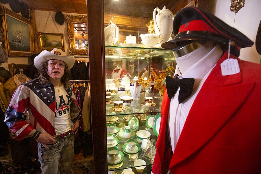 Arnie stands in front of a glass cabinet with intricate vintage tea sets.