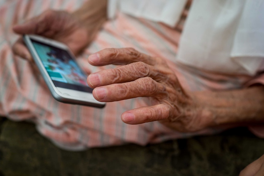 The hand of an older person holds a smartphone.