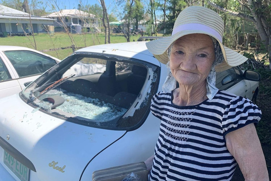 Rosewood resident Robyn McInnes stands next to a car with a smashed rear window after hailstorms.