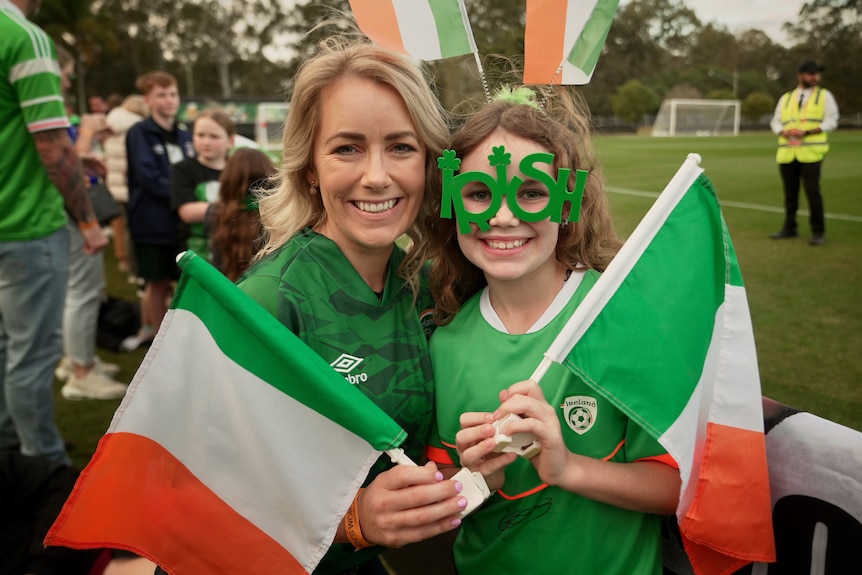 A woman and little girl wearing green and holding flags.