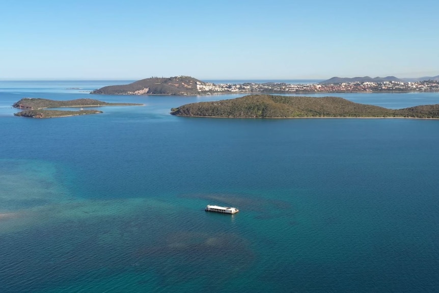 An aerial view showing tuquoise and dark blue waters, a pontoon restaurant, and peninsulas and islands in the background.