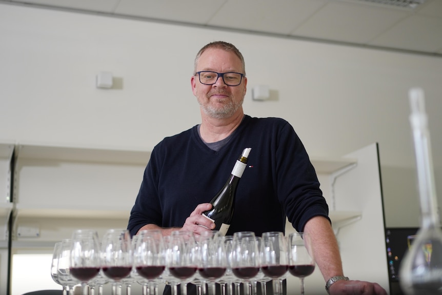 A man holding a wine bottle in front of several filled wine glasses