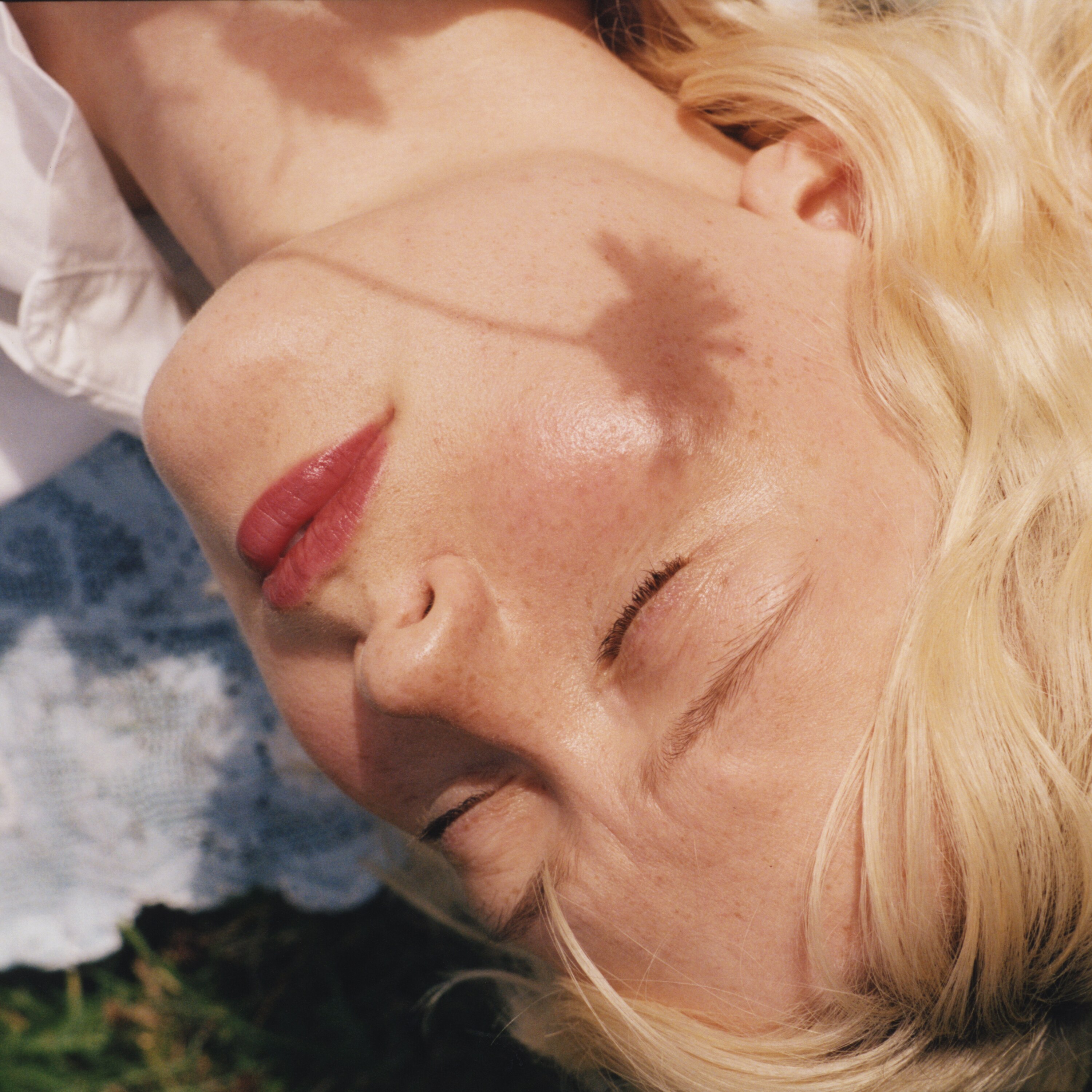 A close up of a white woman with blonde hair and freckles with the shadow of garden flowers on her face