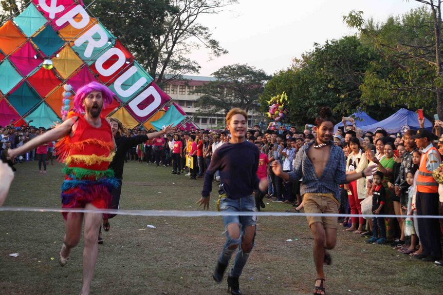 Men in high heels and colourful outfits run towards the finish line