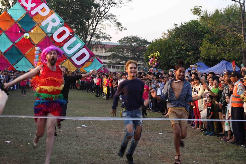 Men in high heels and colourful outfits run towards the finish line