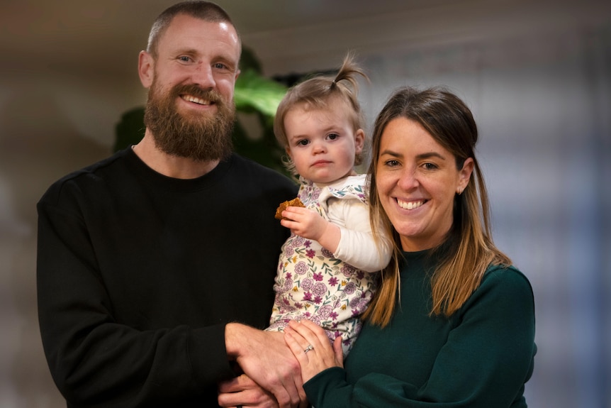 A man and woman smile while holding a little girl.