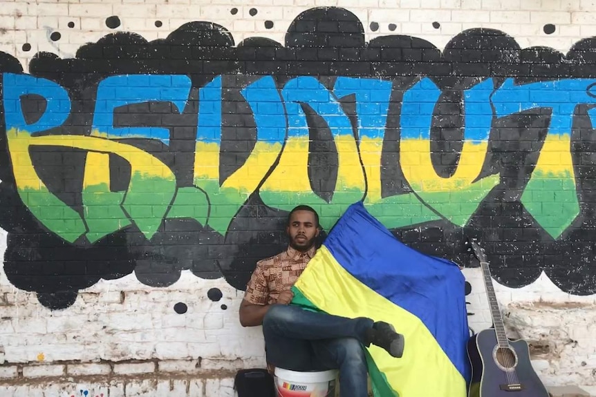 Australia-based Mazin Bashir sits in front of a graffitied wall that reads "Revolution" in Khartoum, Sudan.