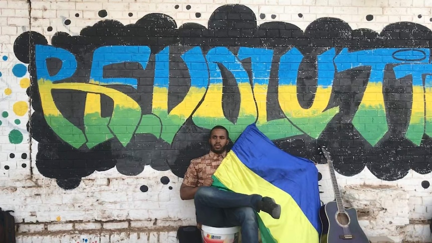 Australia-based Mazin Bashir sits in front of a graffitied wall that reads "Revolution" in Khartoum, Sudan.