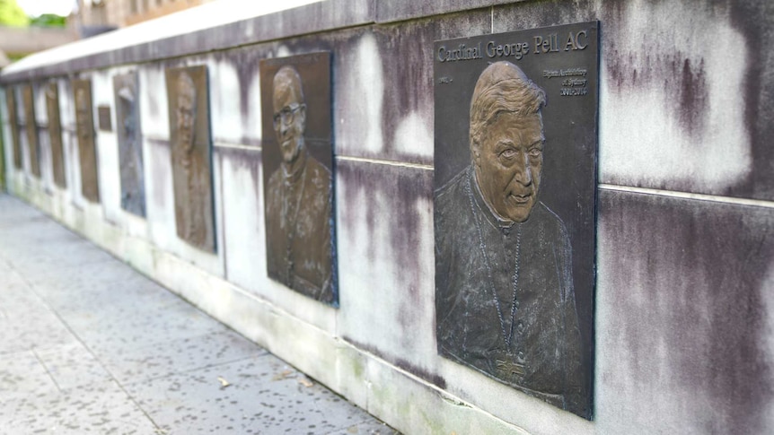a row of plaques with one featuring george pell hanging on a wall