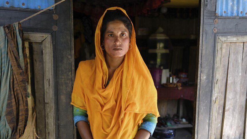 A woman wears an orange shall over her head standing in the doorway of a Bangladesh house 