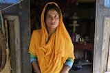 A woman wears an orange shall over her head standing in the doorway of a Bangladesh house 