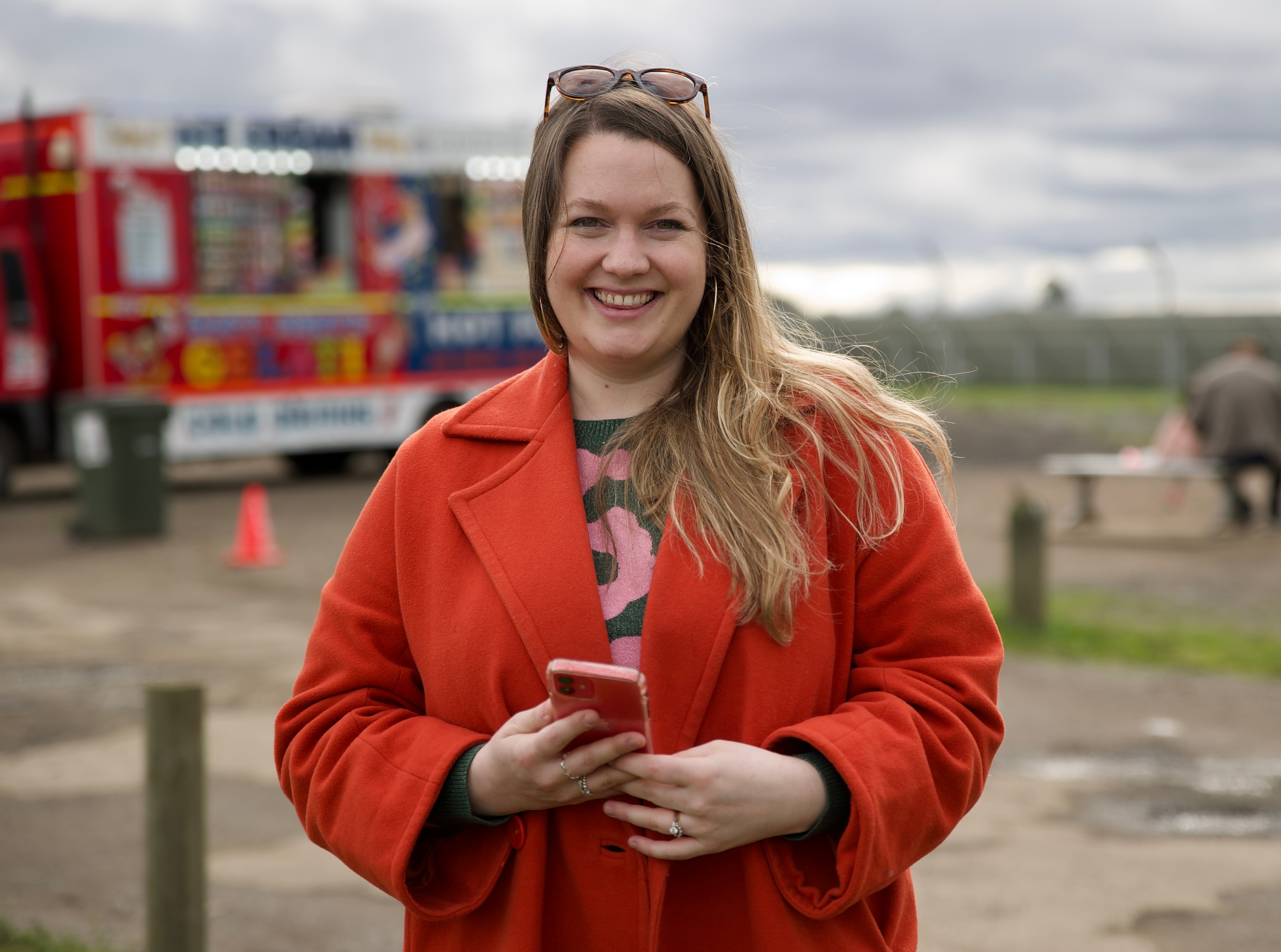a woman is smiling at the camera.  She is holding a phone and wearing a red jacket.