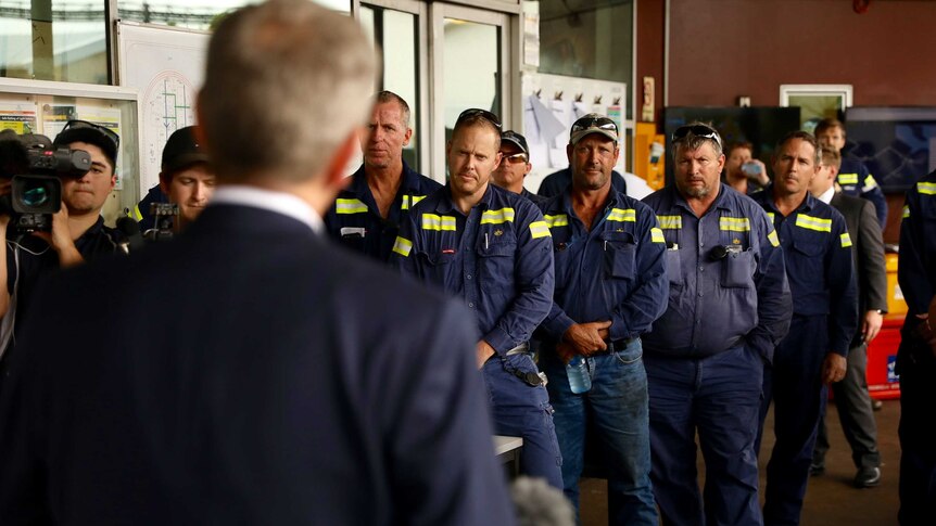 Workers in industrial worktops watch Mr Shorten, who has his back to the camera, as he speaks to them