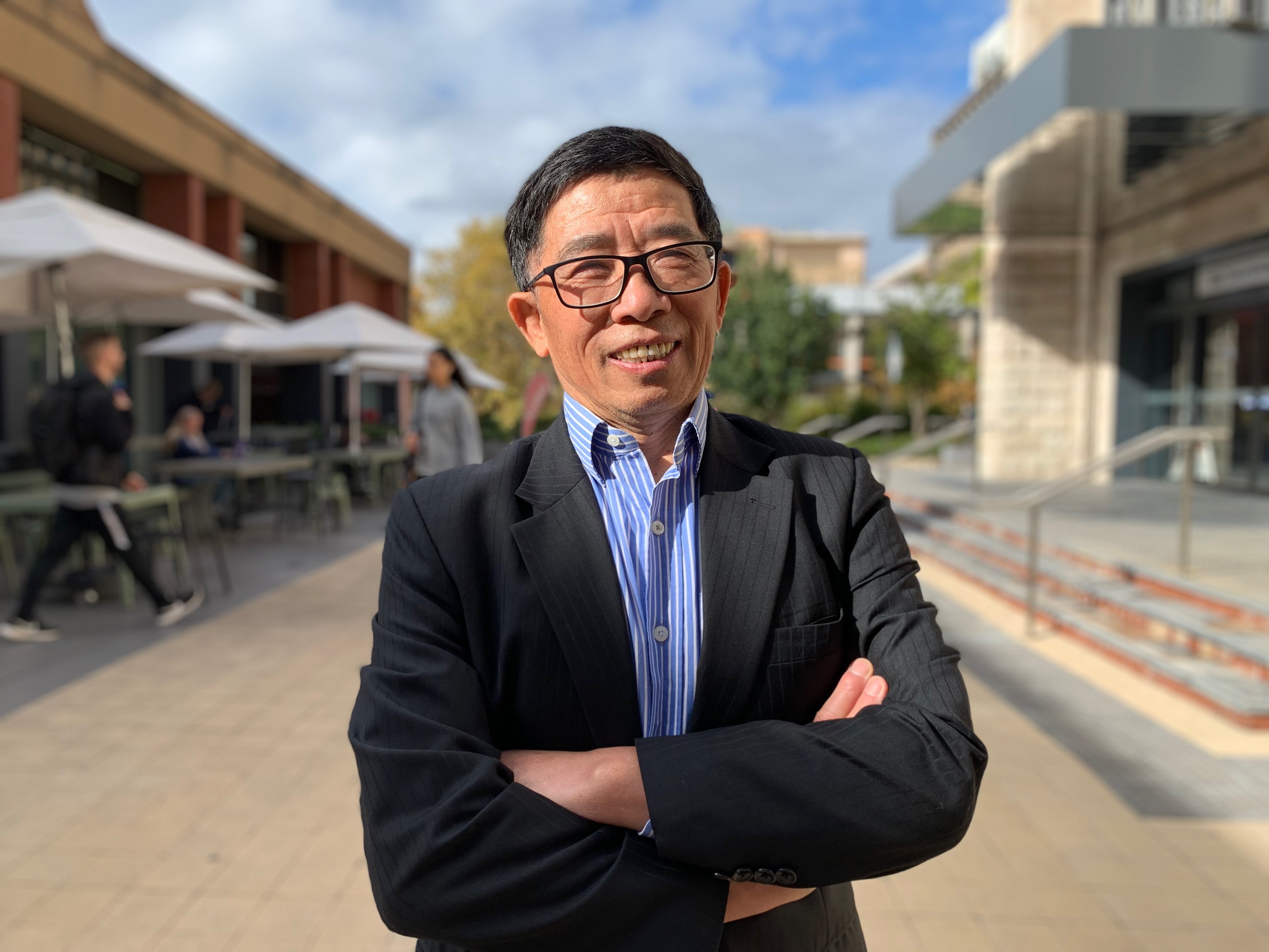 Asian man with black glasses smiling with arms crossed wearing a suit 